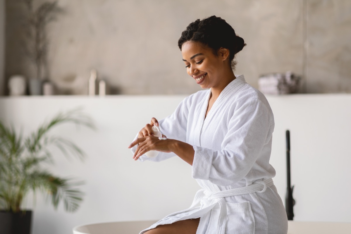 Black woman in luxury spa robe applying skincare in a warm medspa setting